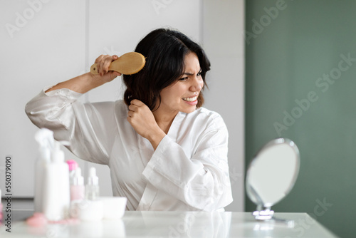 Angry lady brushing dry hair with hairbrush at home