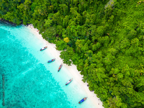 Aerial drone view of famous Monkey Beach at Ko Phi Phi island, Thailand. Tropical beach with white sand, turquoise water and green forest. Long tailed boats are waiting on beach. 