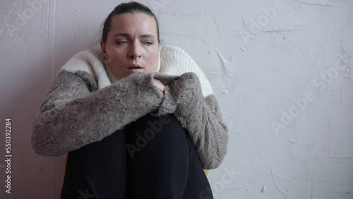 Woman in home room without central heating sitting near white wall. Young girl in warm pullover get warm. Concept of problems with central heating. Flu symptoms, disease, chill, depression