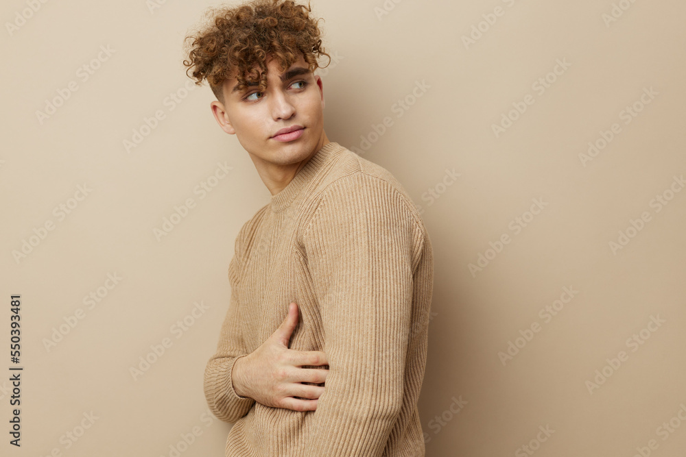 a charming man in a beige sweater stands on a beige background and it's nice to look into the camera with his hand on his body a charming man in a beige sweater stands on a beige background and it's nice to look into the camera with his hand on his body