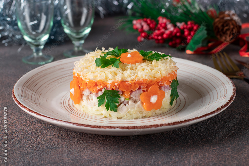 Puff salad with chicken, potatoes, carrots and cheese on a round plate on brown background Puff salad with chicken, potatoes, carrots and cheese on a round plate on brown background