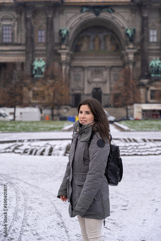 Fototapeta premium Young female tourist walking in the park in front of the Berlin Cathedral with snow all over the ground.