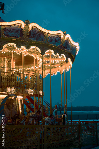 Children's Carousel roundabout, galloper at an amusement park in the evening at night illumination. Outdoor vintage colorful luminous. Blue background. New year, christmas entertainment mood concept.