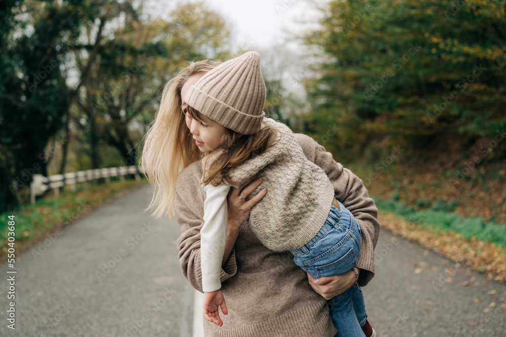 Mom has fun with her little daughter hugging and holding her in her arms on a country road. Mom has fun with her little daughter hugging and holding her in her arms on a country road.