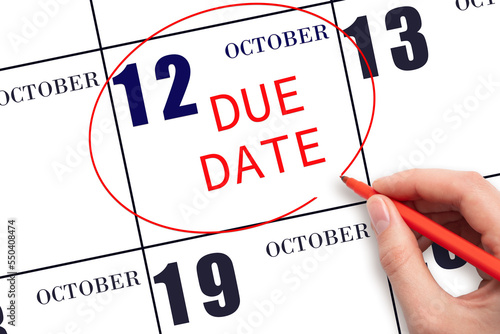 Hand writing text DUE DATE on calendar date October 12 and circling it. Payment due date