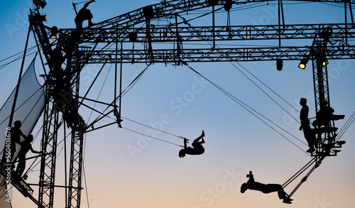 silhouettes of trapeze artists acrobats on the metal scaffolding at sunset photo