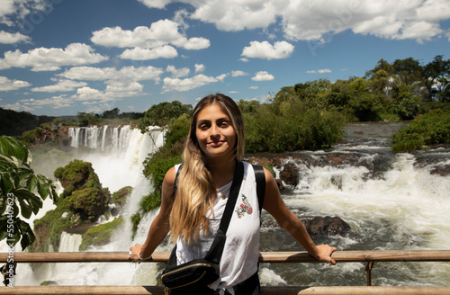 Tourism. Portrait of a young woman with brown hair smiling with the Iguazu waterfalls in the background.