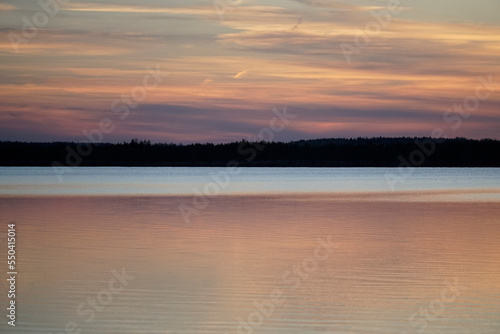 Beautiful sunset in July over a forest lake. Sun  calm quiet waves and reflection 