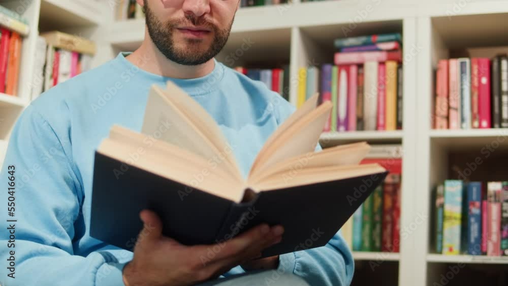 Man reading Book in University Library, Book Shop or Store, Spanish Student Wearing Glasses Standing near Bookshelf Reads Book and Exam Preparations. Man reading Book in University Library, Book Shop or Store, Spanish Student Wearing Glasses Standing near Bookshelf Reads Book and Exam Preparations.