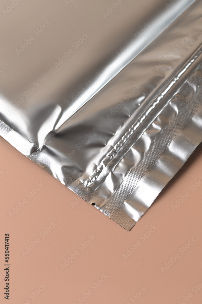 Silver metallic zipper bag with zip lock on beige background. Piece of Aluminum metallic packaging bag Silver metallic zipper bag with zip lock on beige background. Piece of Aluminum metallic packaging bag