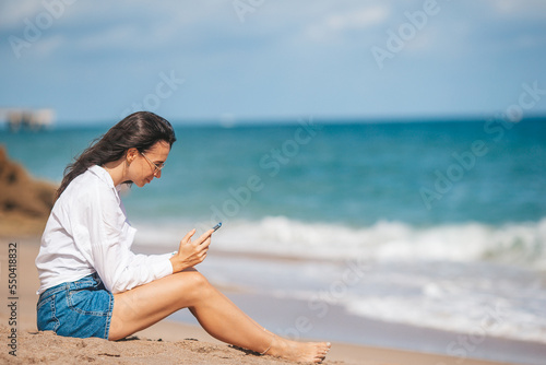 Young woman using mobile phone on the beach. Girl texting in a smartphone on the seashore
