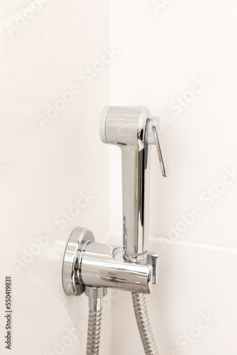 Hygienic shower on white tile wall. Details in bright modern bathroom