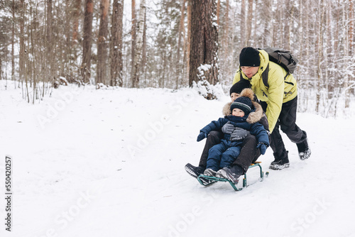 Wallpaper Mural Father with backpack and little sons walking together in winter snowy forest. Happy man and joyful boys sledding and having fun together. Wintertime activity outdoors. Concept of local travel Torontodigital.ca