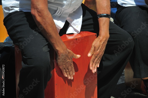 Close-up of a cajon, man's legs and hands are shown as he's playing the instrument in the square of lima peru