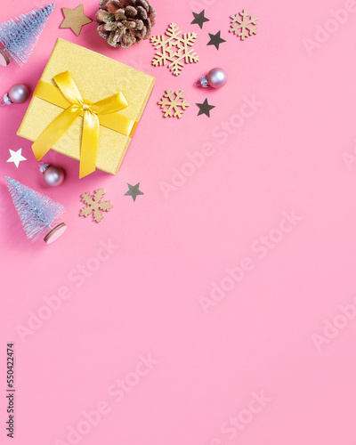 Vertical Christmas card golden gift box with mini Christmas trees and baubles on pastel pink background