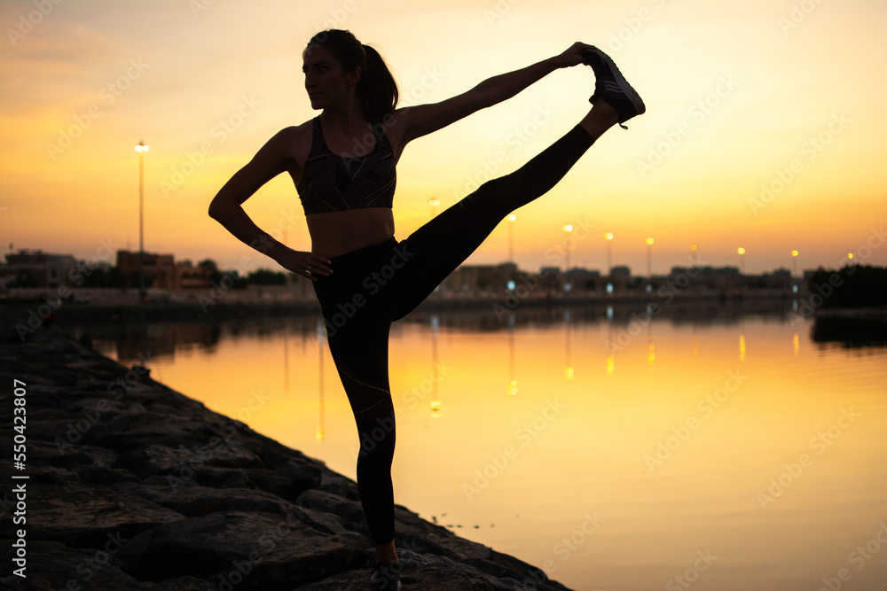 Silhouette of a beautiful yoga woman doing balance exercise at sunrise or sunset near the sea coast.