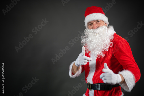  Portrait von einem verkleideten Weihnachtsmann der auf einen Platzhalter zeigt und isoliert vor grauen Hintergrund ist 