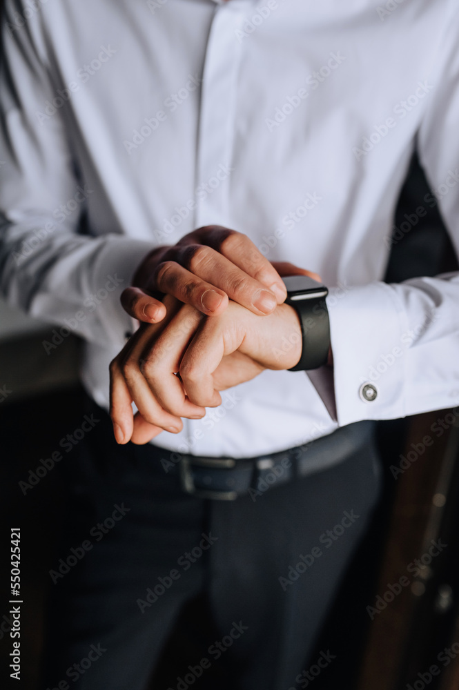 Obraz premium A man, a businessman in a white shirt holds a smartwatch, a wristwatch on his hand, preparing in the morning. Photography, business.