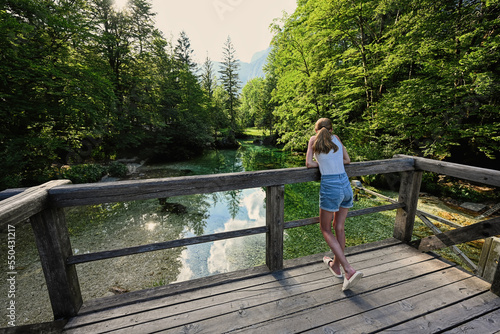 Back of girl stand in wooden bridge of emerald green water river Sava Bohinjka in Julian Alps, Ukanc, Slovenia.