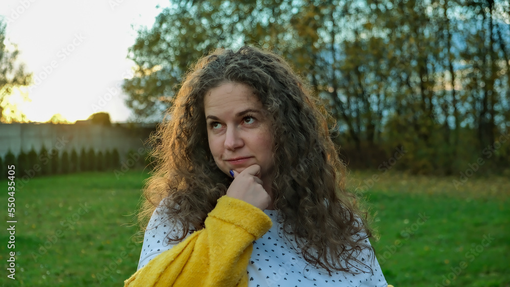 A young beautiful curly girl thought against the background of the forest