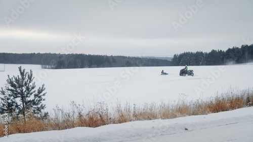 Winter fun. Tubing. Dad rides his child on an inflatable sled behind a Quad bike, snowmobile on a snow-covered field against the background of a forest. High quality 4k footage