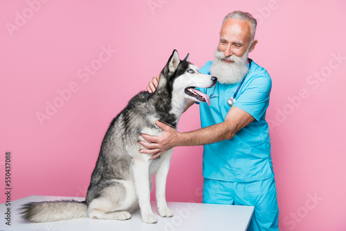 Full size photo of careful positive optimistic doctor wear blue uniform husky sitting on table checkup isolated on pink color background