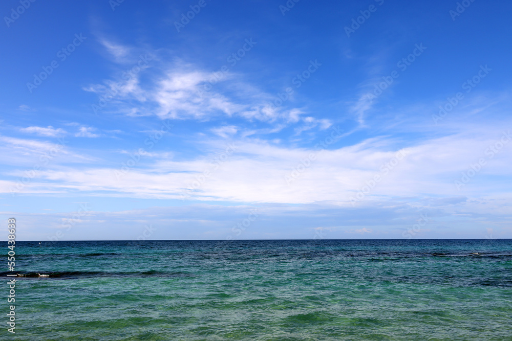 Beach by the sea with emerald green sea water and blue sky and white clouds. Summer vacation on tropical paradise beach concept. Ripple of water splash. Summer vibes.