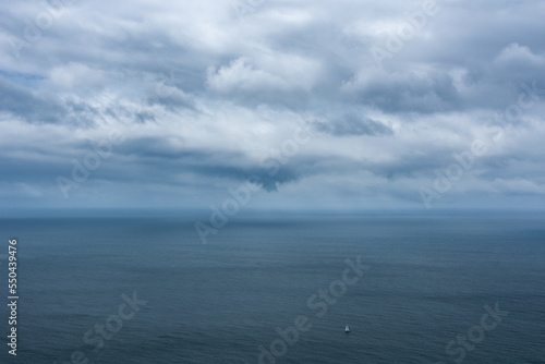 Ein einsames Segelschiff treibt mitten auf dem Ozean und über ihm dicke graue Regenwolken