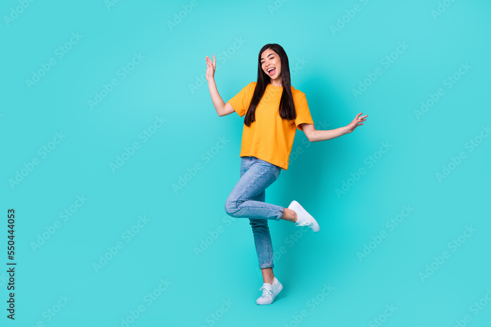 Full body photo of cute brunette lady dance wear orange t-shirt jeans shoes isolated on teal color background