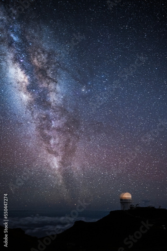 The Milky Way and stars at night over the observatory at Mt. Haleakala in Maui, Hawaii with clouds below.