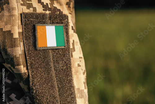 Close up millitary woman or man shoulder arm sleeve with Cote d'Ivoire Ivory Coast flag patch. Troops army, soldier camouflage uniform. Armed Forces, empty copy space for text