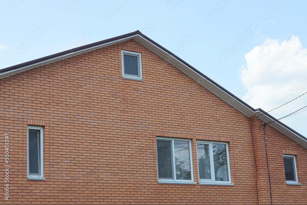 one large brown brick attic of a private house with white windows on the street against a blue sky