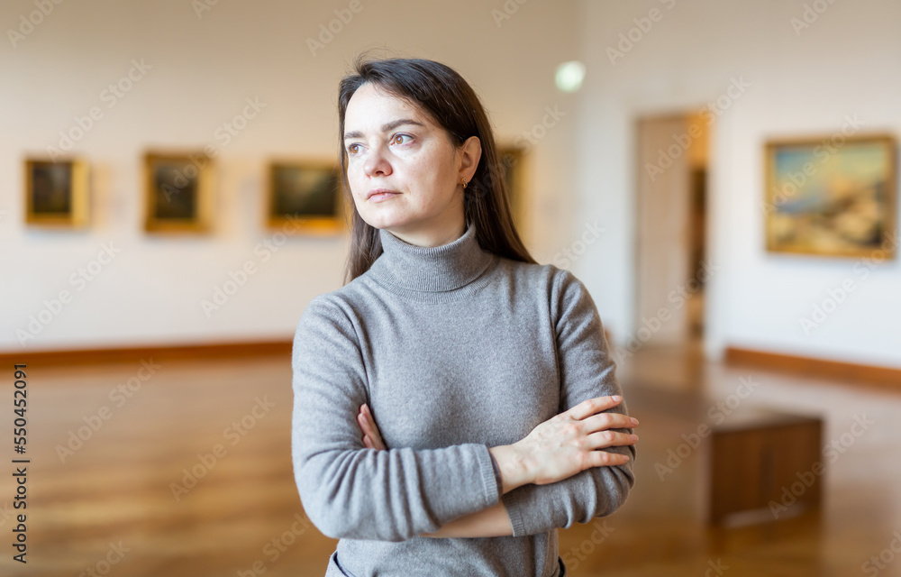 Obraz premium Positive brunette admiring artworks at paintings exposition walking in spacious museum hall..