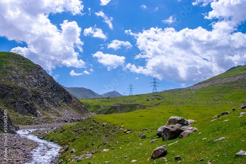 Fényképezés Electric towers stand on the green hillside which crossing by mountain rill surr
