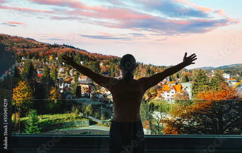 Man with arms outstretched in balcony against towm in autumn