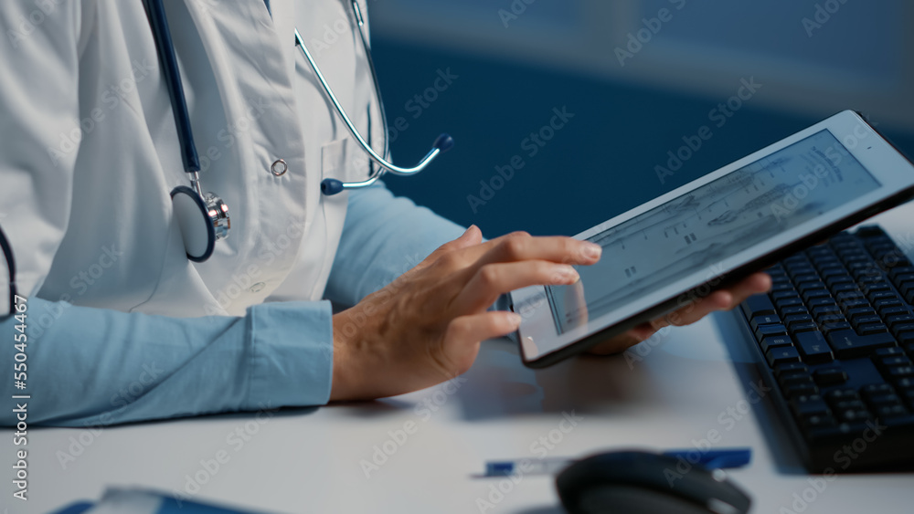 Close up of general practitioner holding tablet computer analyzing radiography while working over hours at medical expertise in hospital office. Doctor planning medication treatment for patient Close up of general practitioner holding tablet computer analyzing radiography while working over hours at medical expertise in hospital office. Doctor planning medication treatment for patient