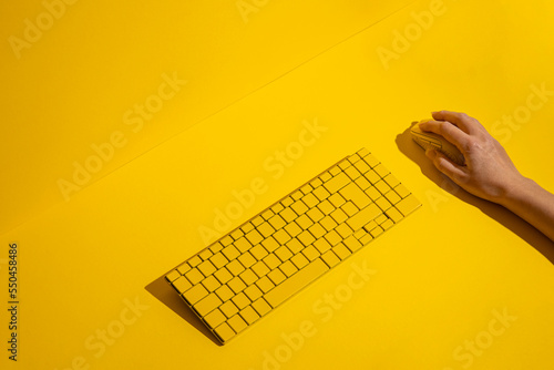 Female hand holds a yellow wireless mouse and keyboard on a blue background. Top view, flat lay