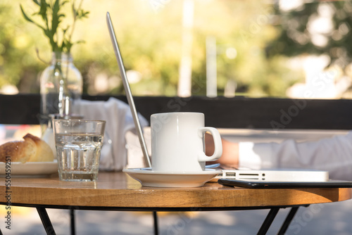 person sitting outdoors working on their laptop, cup of coffee on the table