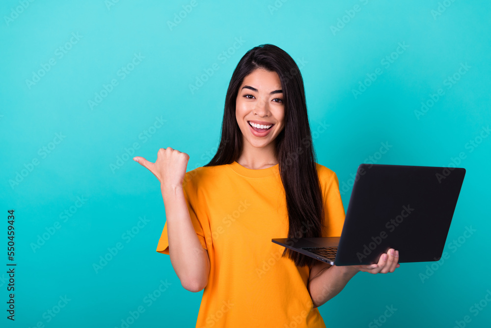 Photo of cute millennial lady index empty space hold laptop wear orange t-shirt isolated on teal color background Photo of cute millennial lady index empty space hold laptop wear orange t-shirt isolated on teal color background