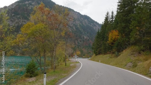 Car with camera driving next to Plansee lake in Austria. Beautiful road, autumn forest, high mountains and clear lake are in the camera shot.