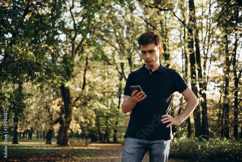 a man on a walk in the autumn park looks at his mobile phone