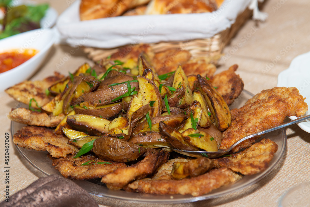 Countryside dish, fried, grilled potato with and meat pieces, chiken chops, spices and green cutted parsley in glass plate on table with light tablecloth. Homemade food. Soft focus. Countryside dish, fried, grilled potato with and meat pieces, chiken chops, spices and green cutted parsley in glass plate on table with light tablecloth. Homemade food. Soft focus.