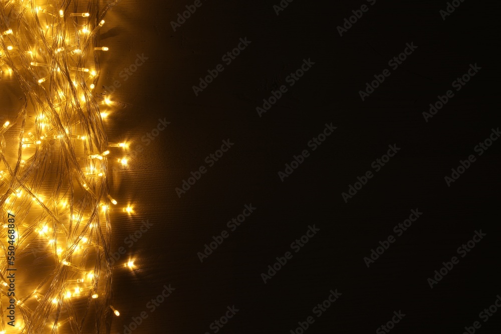 Fototapeta premium Beautiful glowing Christmas lights on wooden table, top view. Space for text