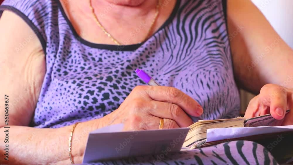 Old woman calculating bills expenses for the month. Old woman writing details about the bills expenses in the notebook. Senior woman with bills Old woman calculating bills expenses for the month. Old woman writing details about the bills expenses in the notebook. Senior woman with bills