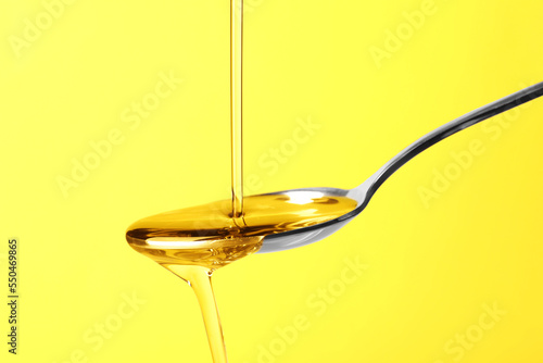Pouring cooking oil into spoon on yellow background, closeup