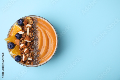 Bowl of delicious fruit smoothie with fresh orange slices, blueberries and granola on light blue background, top view. Space for text