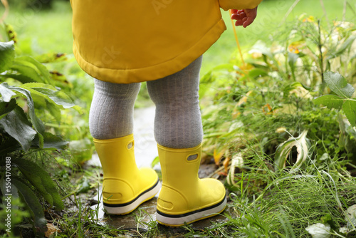 Little girl wearing rubber boots standing in puddle outdoors, closeup. Back view