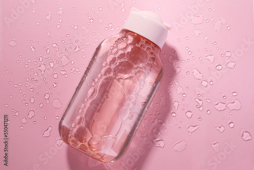 Wet bottle of micellar water on pink background, top view photo