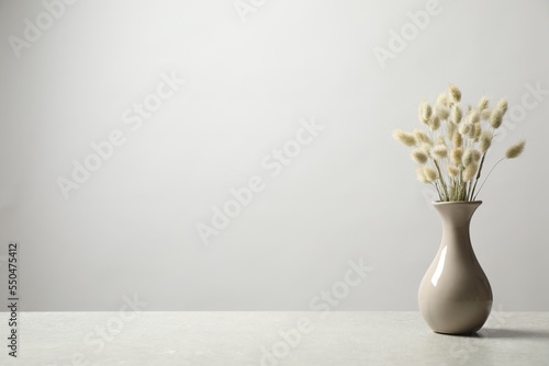 Dried flowers in vase on table against light background. Space for text