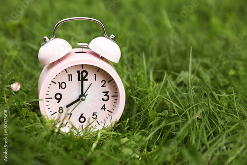 Pink alarm clock on green grass outdoors, space for text